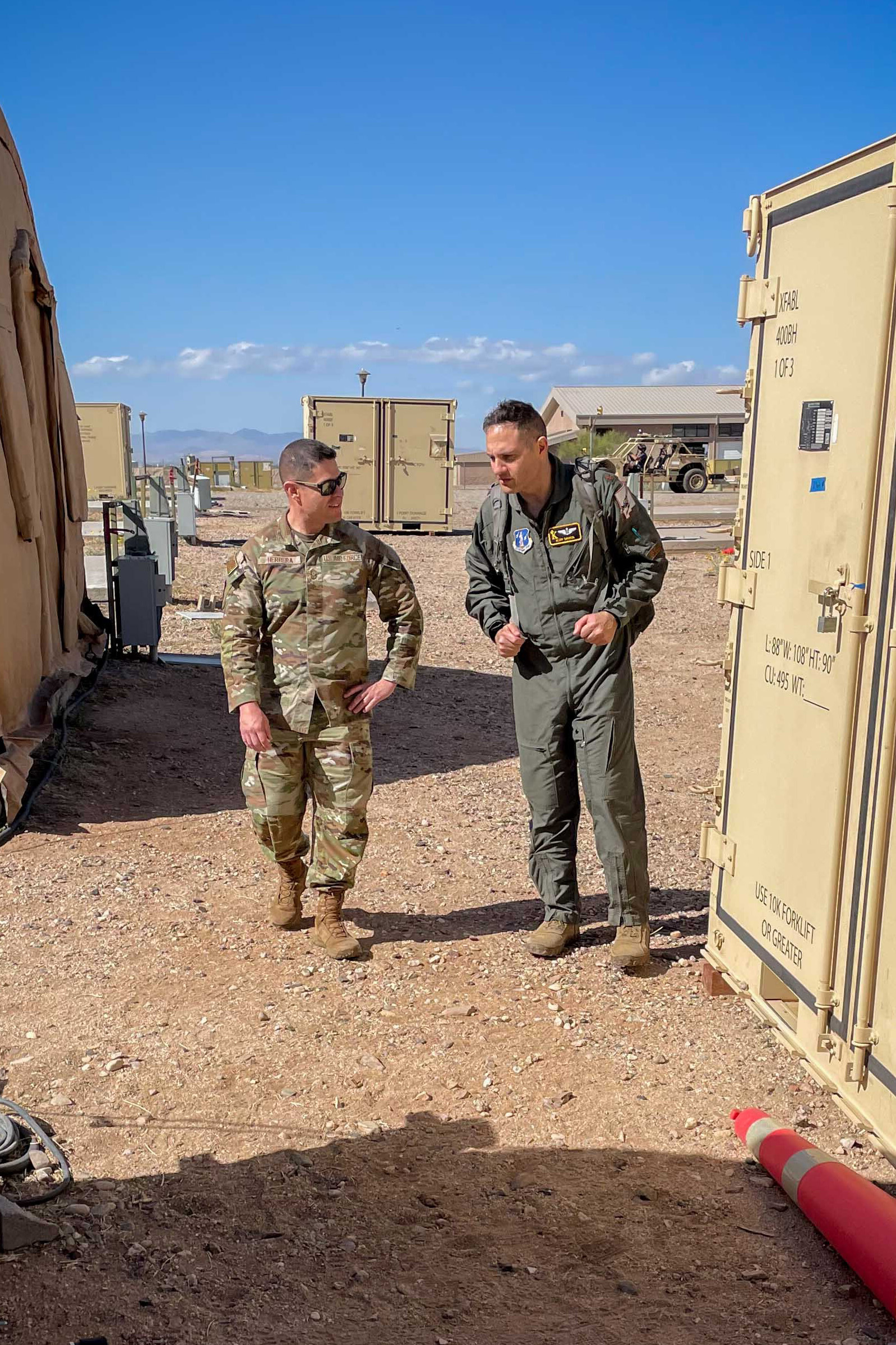 Two airmen confer between tents and equipment containers