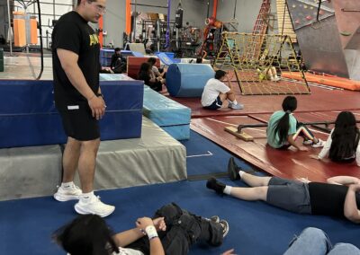 Youth participants rest on training mats during a physical fitness session at an obstacle course facility