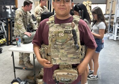 Youth tries on a tactical plate carrier during a hands-on military equipment demonstration